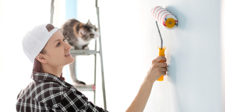 Girl painter, designer and worker paints a roller and brush the wall